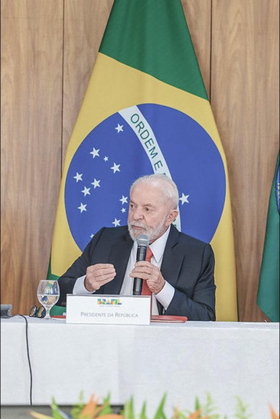 President Lula speaks into a microphone at the meeting of the National Council for Science and Technology, in front of the Brazilian flag